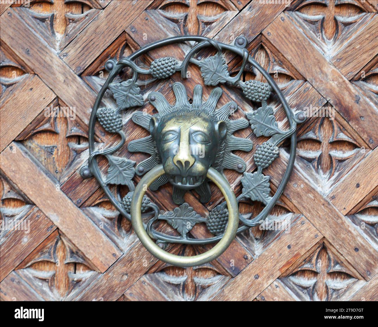 MALBORK, POLAND - 6 NOVEMBER 2023: An ornamental brass and iron door knocker on an intricately carved wooden door in the world's largest Stock Photo