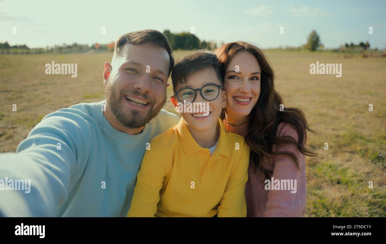 Happy wide smiling Caucasian family father mother son little boy child kid posing mobile phone looking camera taking selfie photo outside rural field Stock Photo