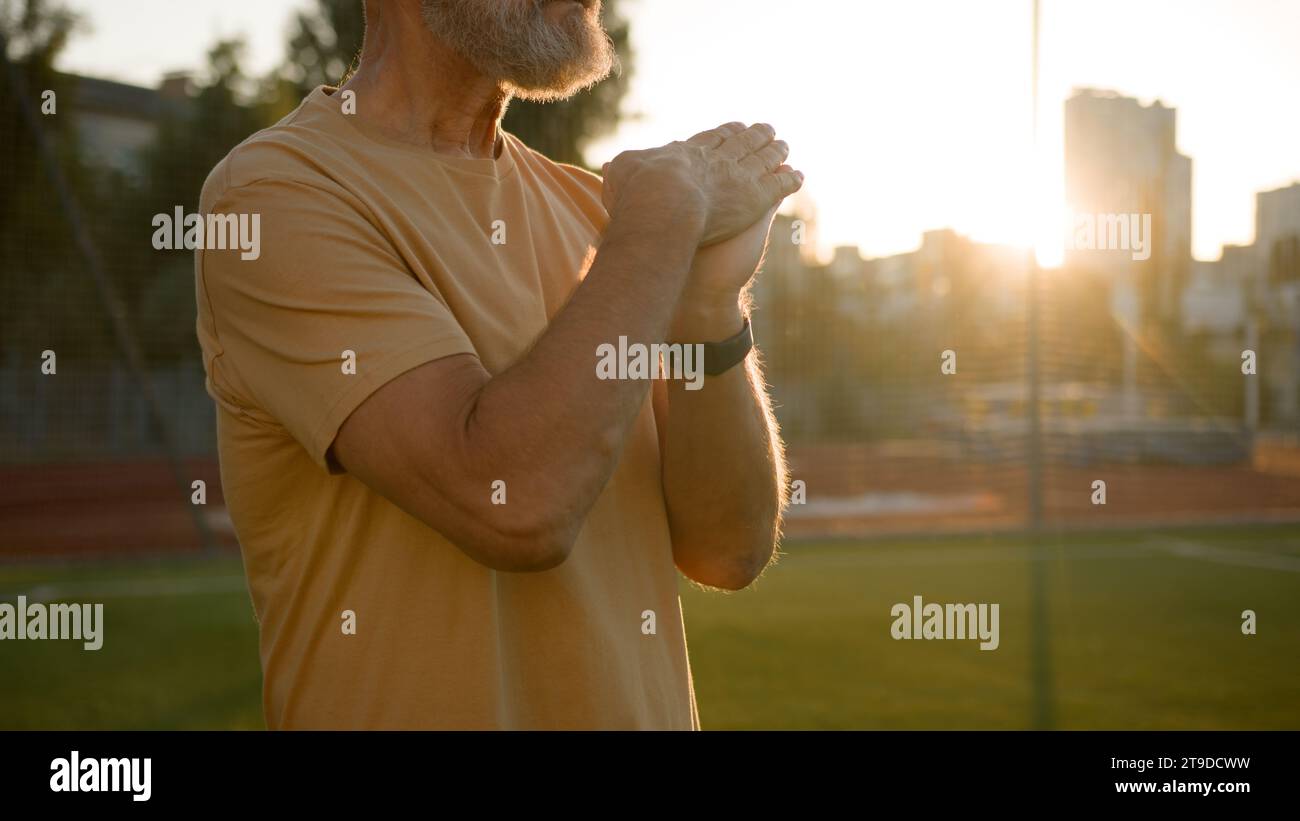 Caucasian elderly man stretching arms hands warm up exercises sport pensioner city outdoors sunrise nature morning fitness training health care old Stock Photo