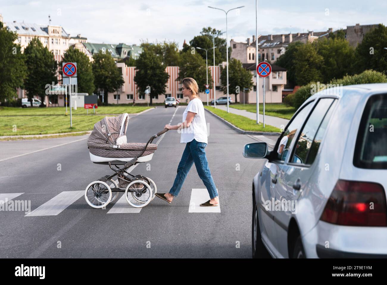 Young mother with the baby pram is walking by the crosswalk. Concepts of safety and traffic code. Stock Photo