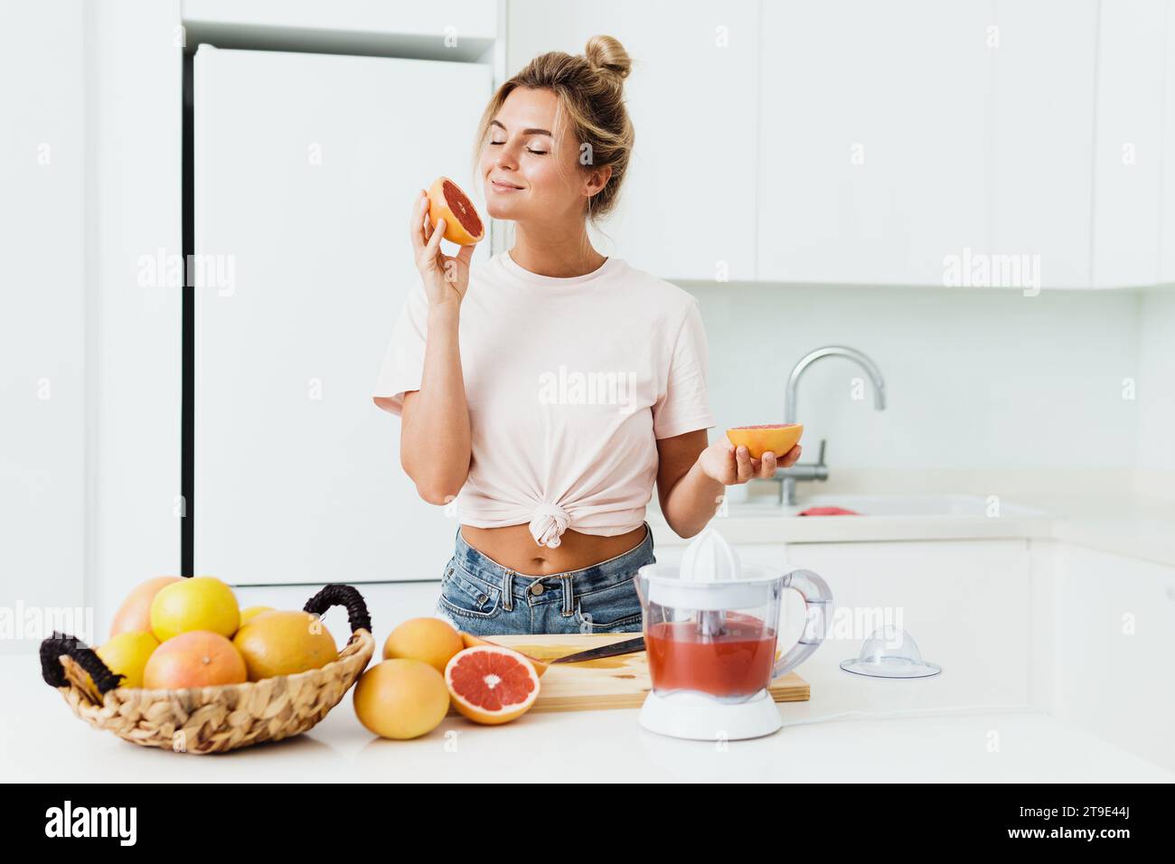 Young beautiful woman sniffing fresh grapefruit during citrus juice preparation at home Stock Photo