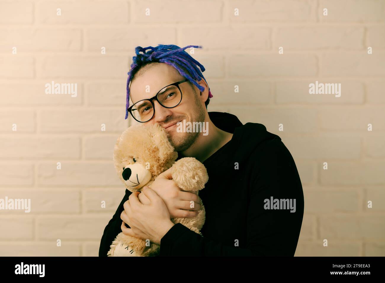 The Tender Embrace: A Man with Dreadlocks with Glasses Cherishing a Plush Toy. Stock Photo