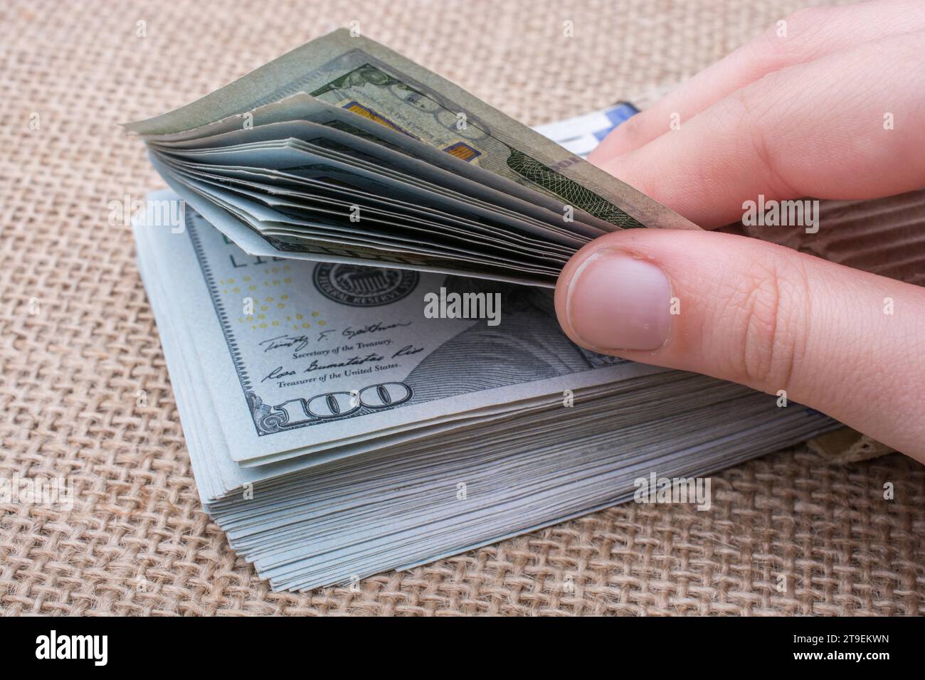 Hand holding banknote bundle of US dollar on a linen canvas background ...