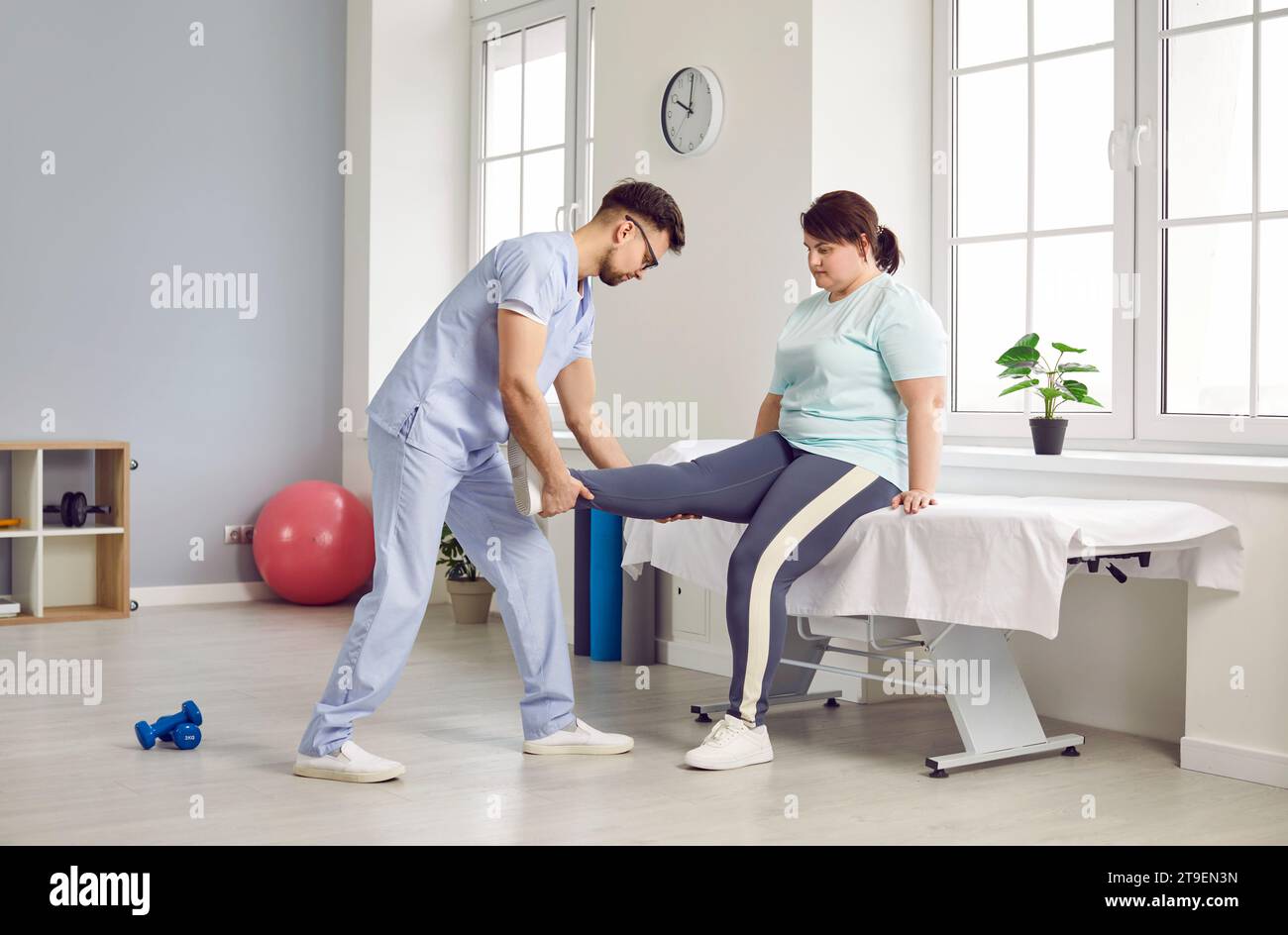 Doctor massaging leg muscles of fat woman who is undergoing physiotherapy treatment at clinic