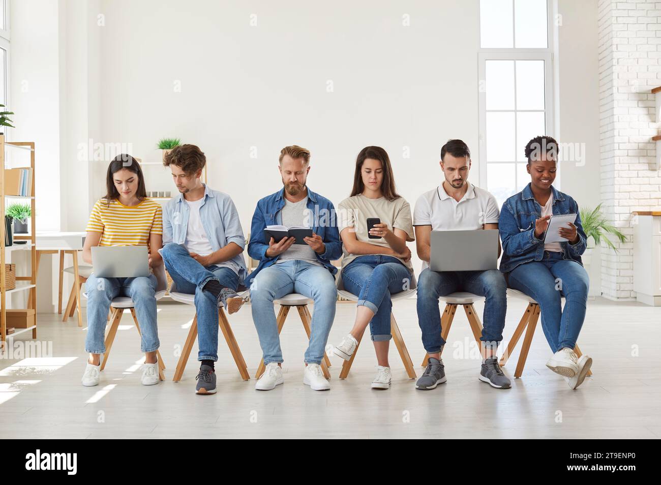 Multicultural young people using digital devices sitting in row Stock Photo