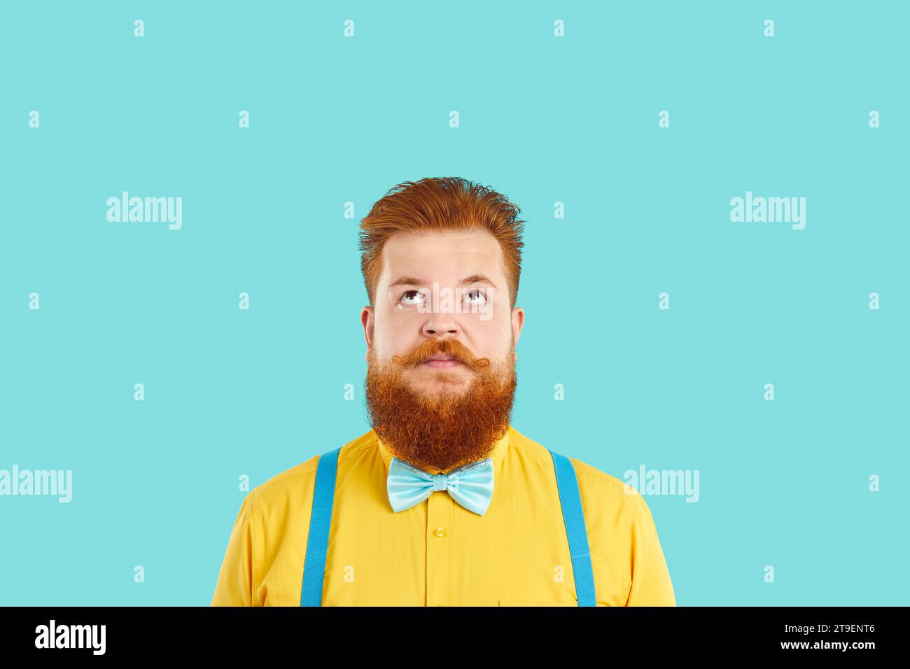 Funny redbeard Caucasian man looks up at empty copy space, stands on turquoise background Stock Photo