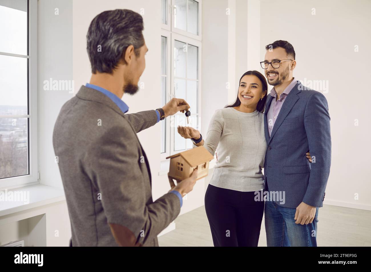 Real estate agent giving house key to a young happy smiling couple ...