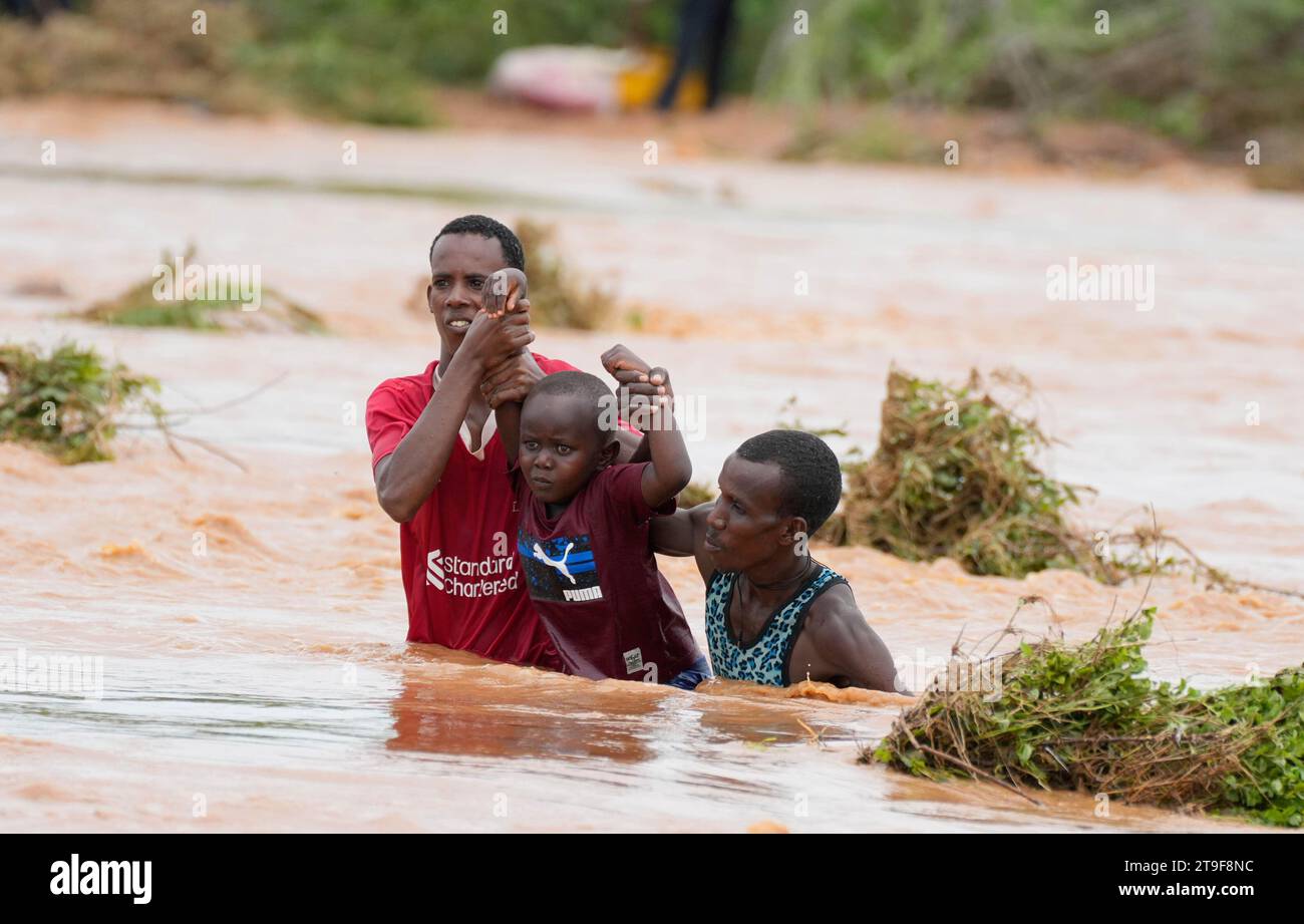 Residents help a young child while trying to cross a road damaged by El Niño rains in Tula, Tana River county in Kenya on Saturday, Nov. 25, 2023. Severe flooding in the country has killed at least 71 people and displaced thousands, according to estimates from the UN Office for the Coordination of Humanitarian Affairs. (AP Photo/Brian Inganga) Stock Photo