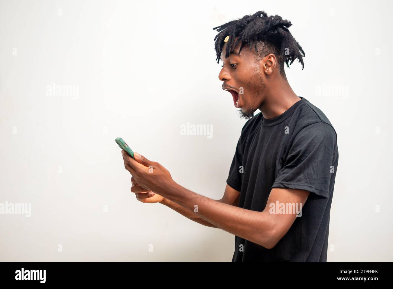 photo of young black guy on dreadlocks sending message on mobile phone. Happy African-American man using smartphone, enjoying chatting online, messagi Stock Photo