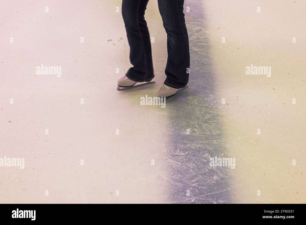 View of woman's legs in jeans and white figure skates standing on ice at ice rink Stock Photo