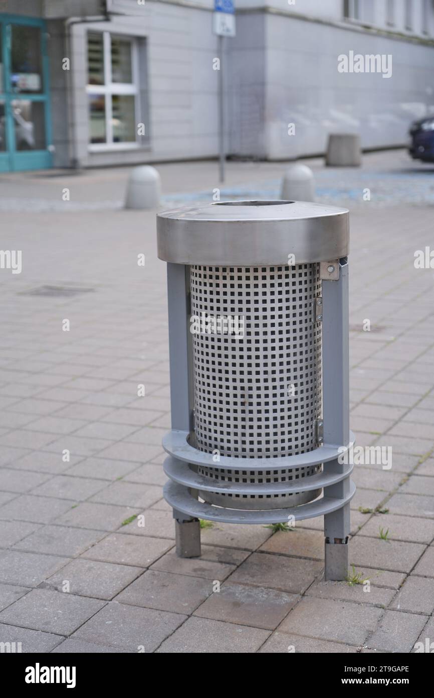 Single modern metal trash bin on a concrete sidewalk with a light grey concrete building, outdoor urban city scape with a trash can on the street Stock Photo