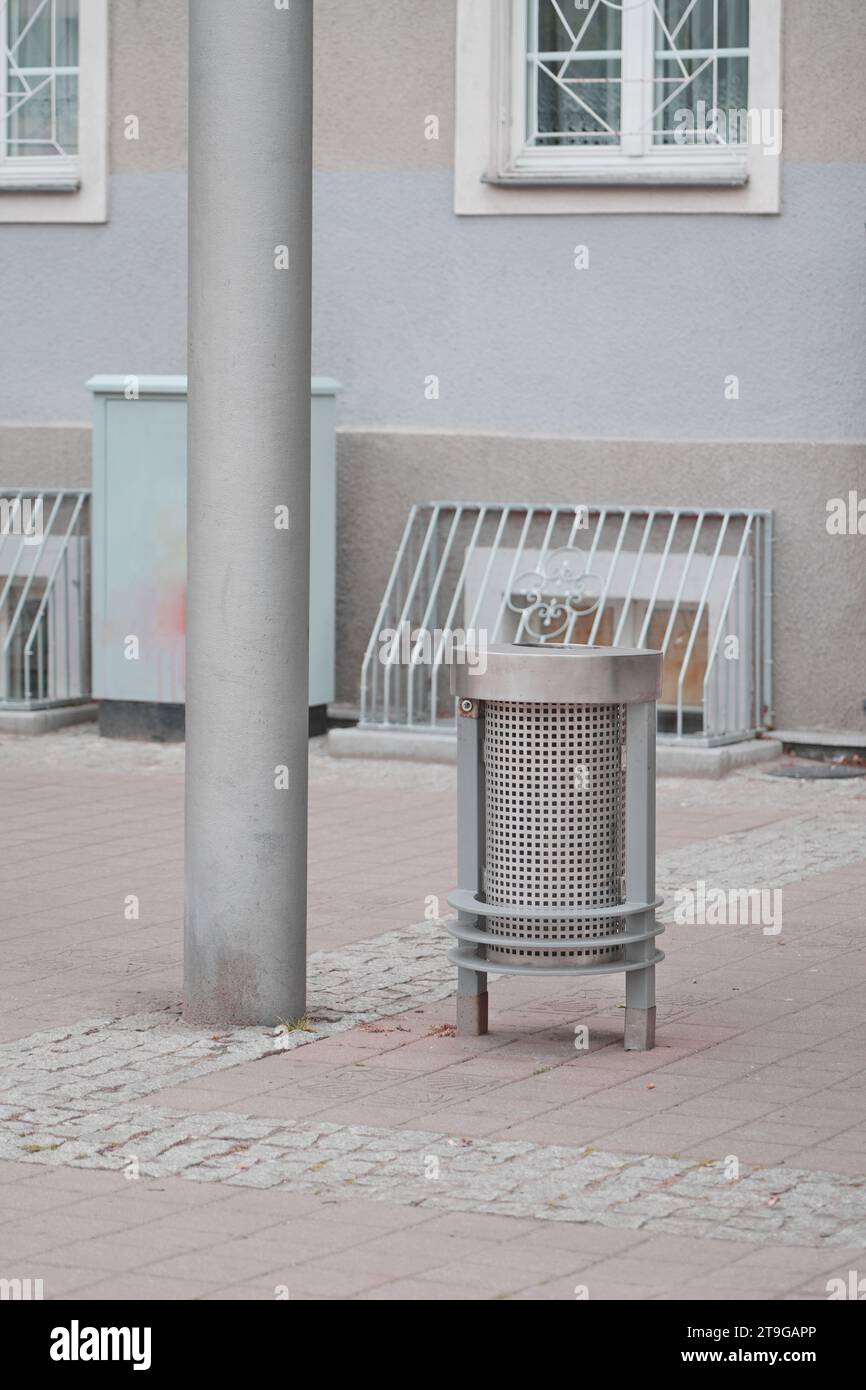 Single modern metal trash bin on a concrete sidewalk with a light grey concrete building, outdoor urban city scape with a trash can on the street Stock Photo