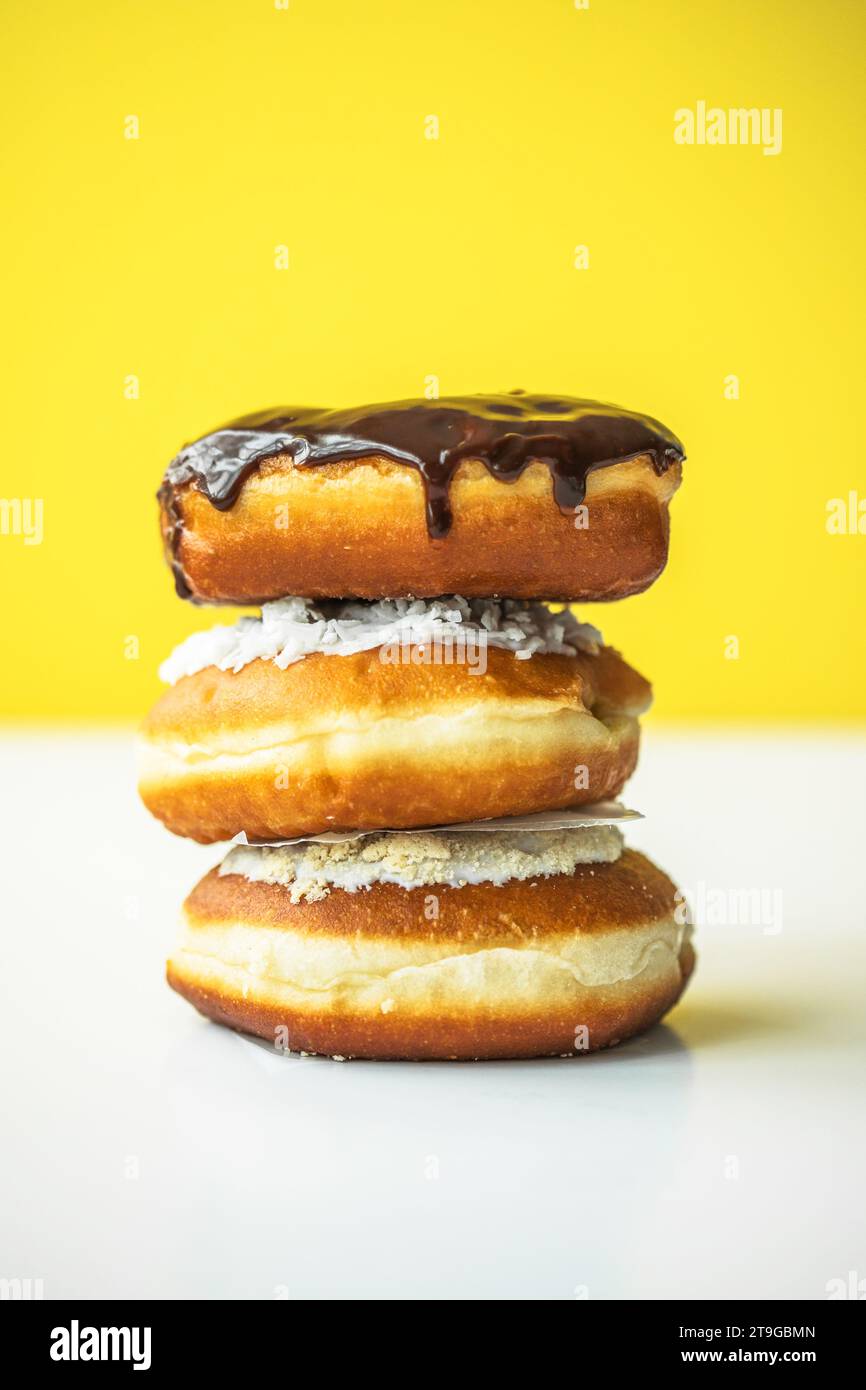 Sweet donuts of different bright colors lie in a large pile on a colored background Stock Photo