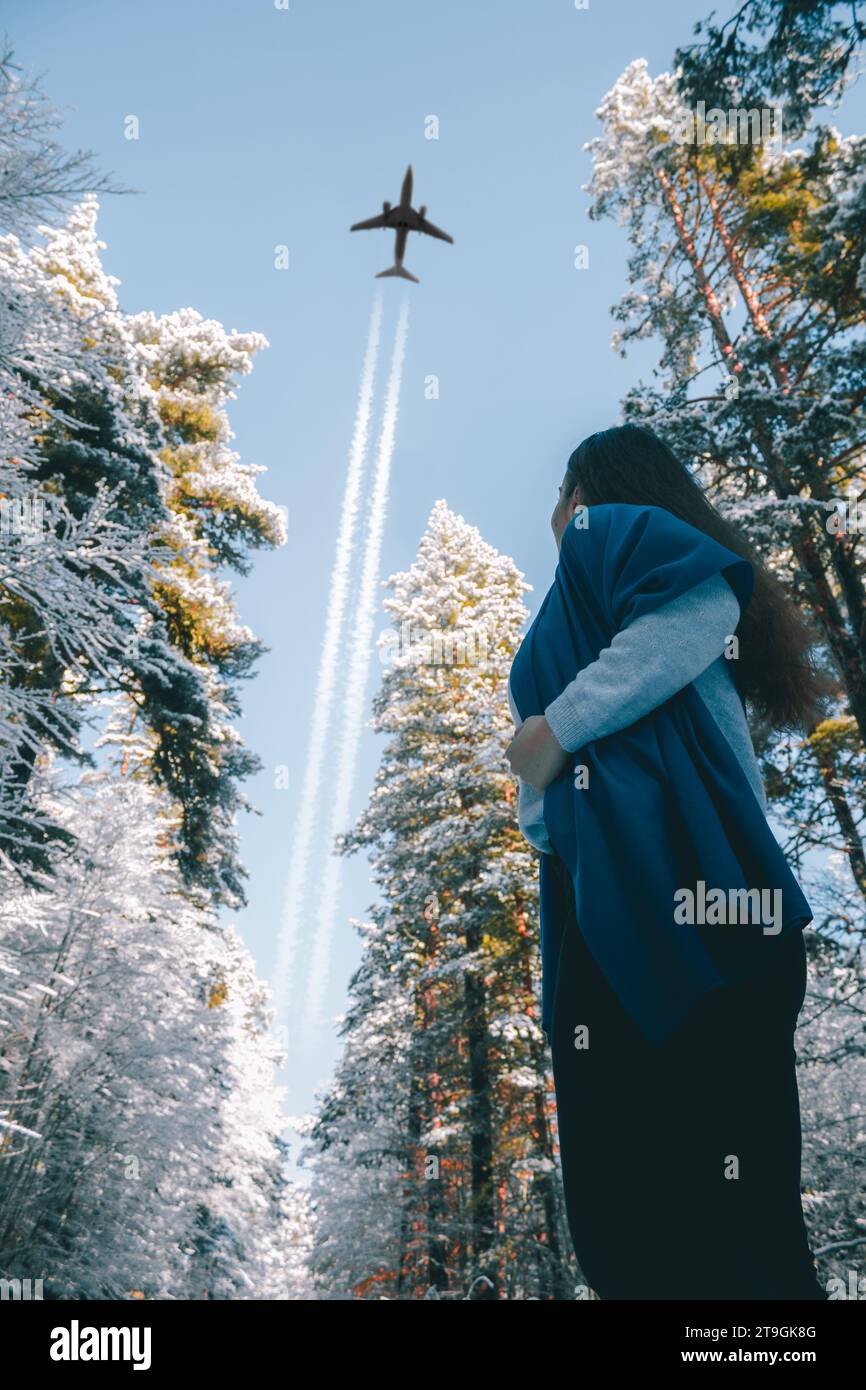 Bulgaria - 11 22 2023: A young girl posing for a low angle photo of her looking in the sky with a plane above the trees. Stock Photo