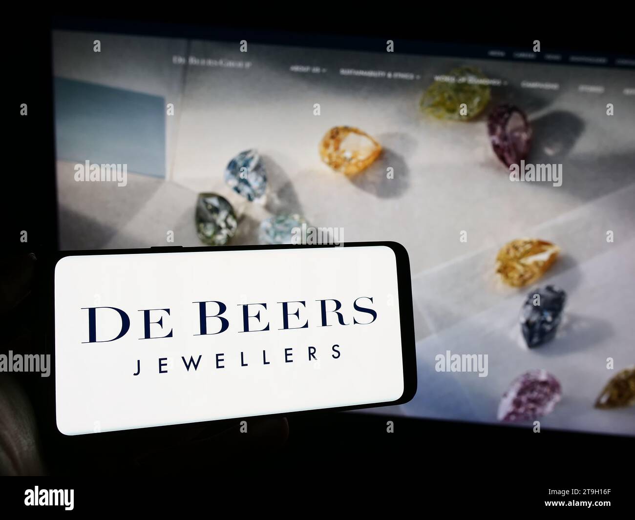 Person holding cellphone with logo of diamond mining and trading company De Beers Group in front of business webpage. Focus on phone display. Stock Photo