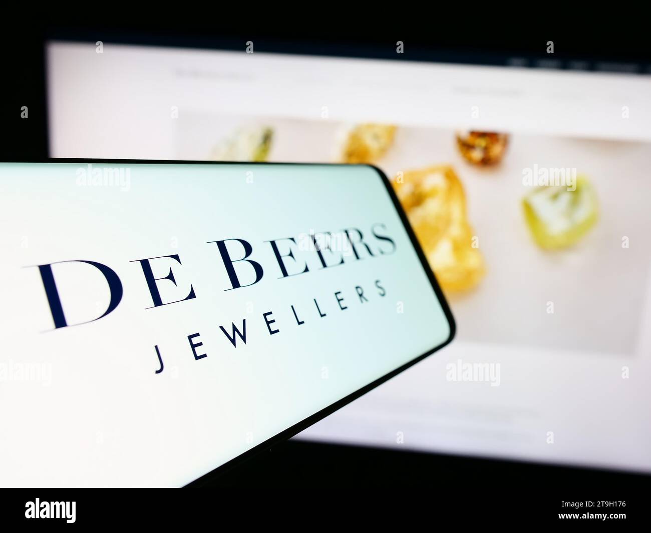 Cellphone with logo of diamond mining and trading company De Beers Group in front of business website. Focus on center-left of phone display. Stock Photo