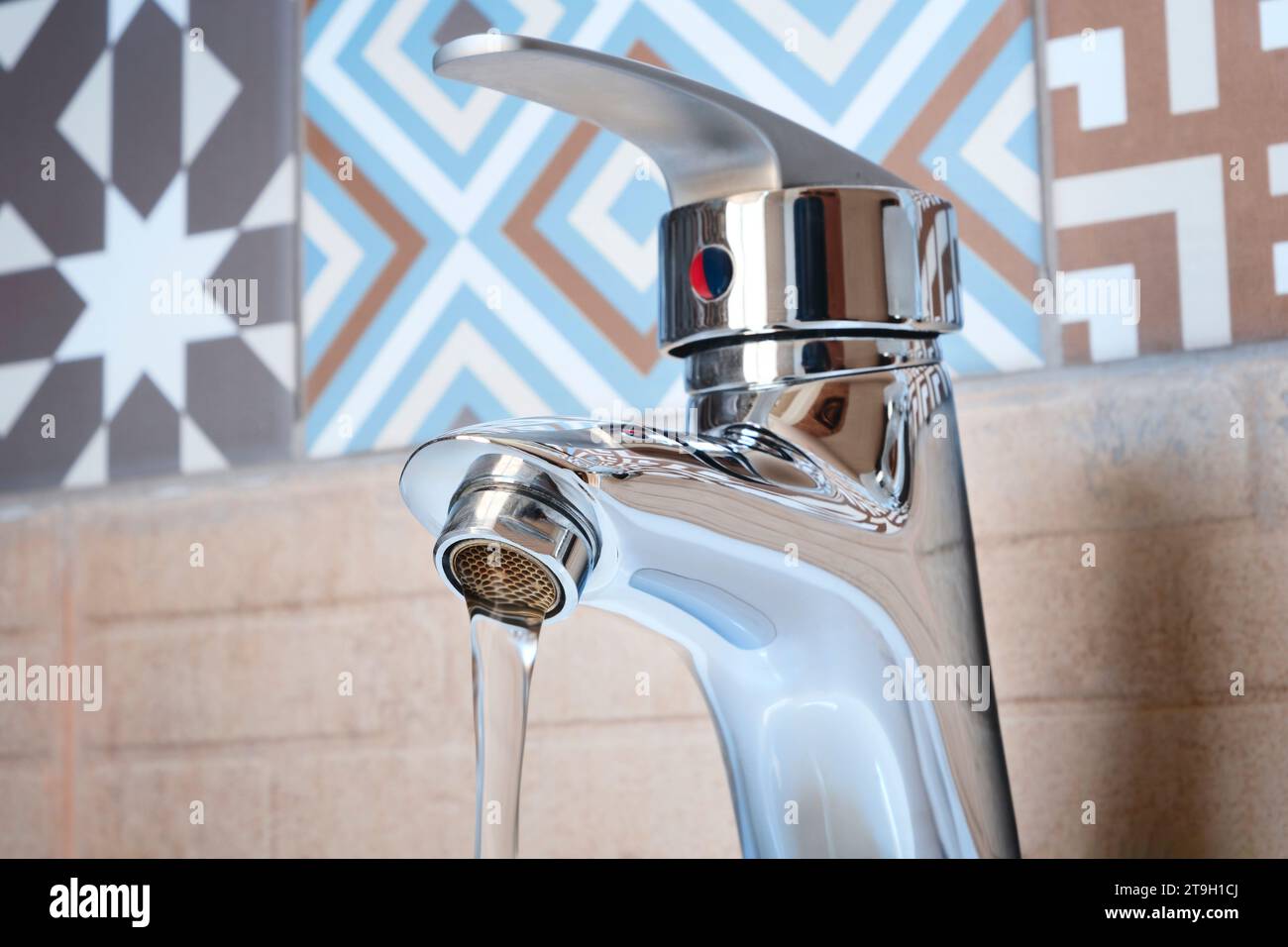 Modern chrome faucet with water flow in bathroom interior, sanitation