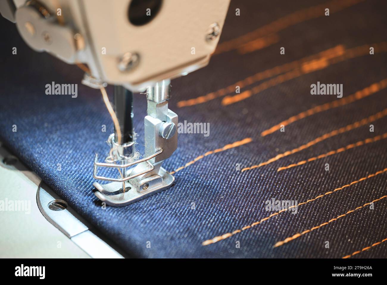 Sewing machine sews blue denim with orange threads closeup Stock Photo