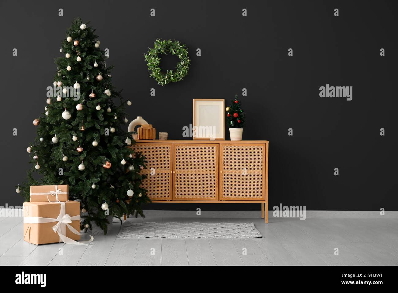 Beautiful Christmas tree with gifts and wooden dresser near dark wall. Banner for design Stock Photo