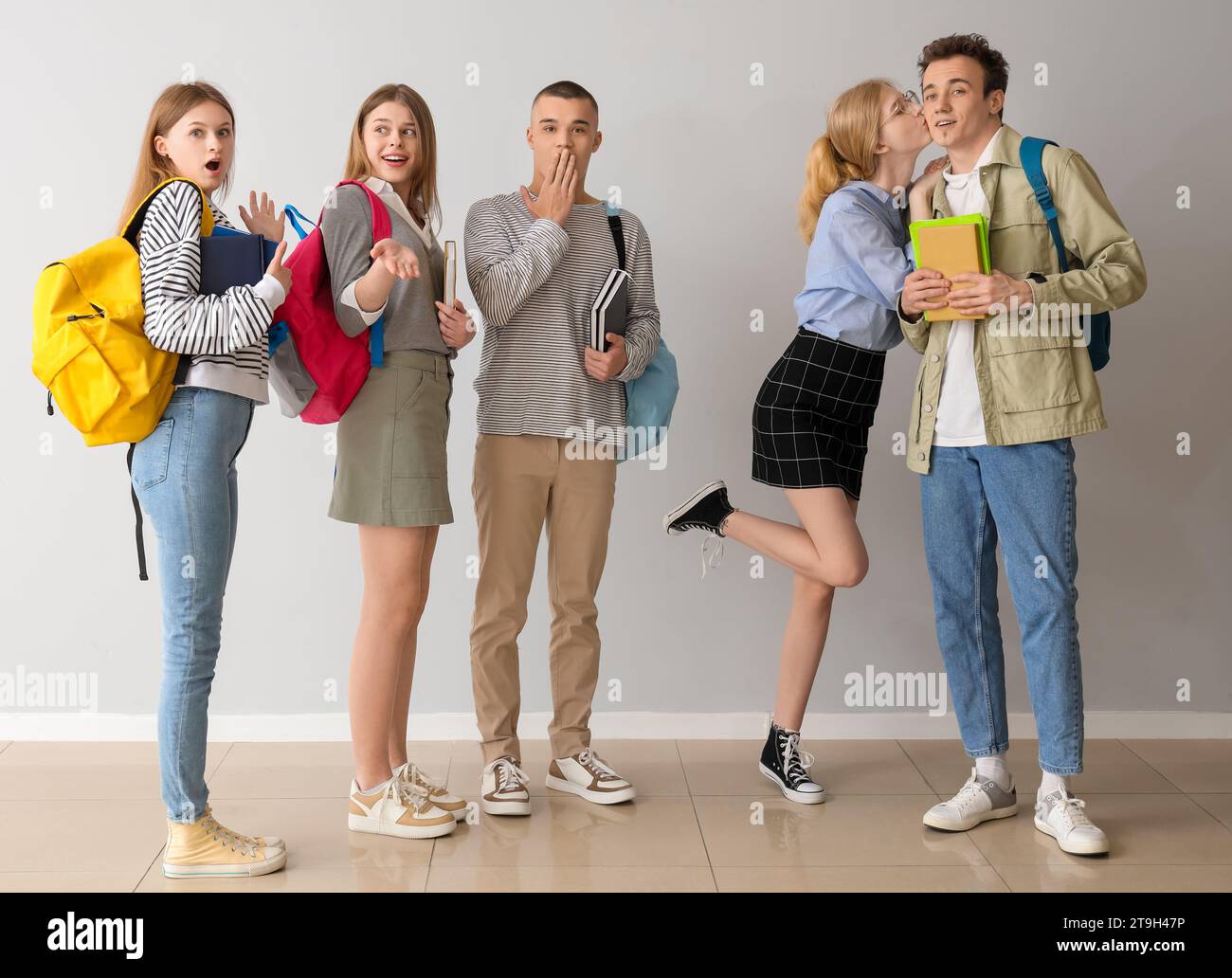 Group of students and their kissing friends near grey wall Stock Photo