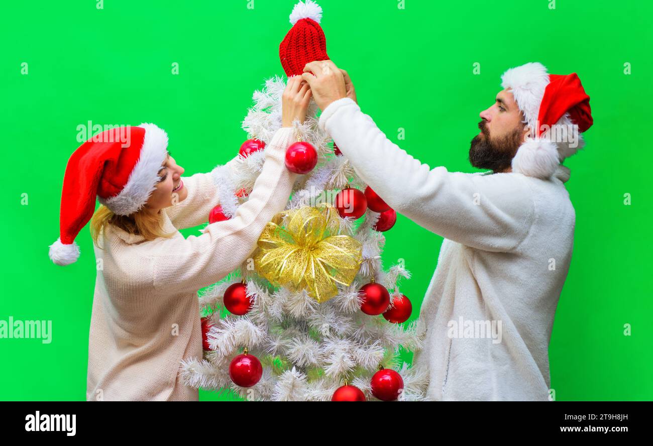 Christmas couple man and woman in Santa hat decorating Christmas tree together at home. Winter holidays. Christmas or New Year celebration. Holiday Stock Photo