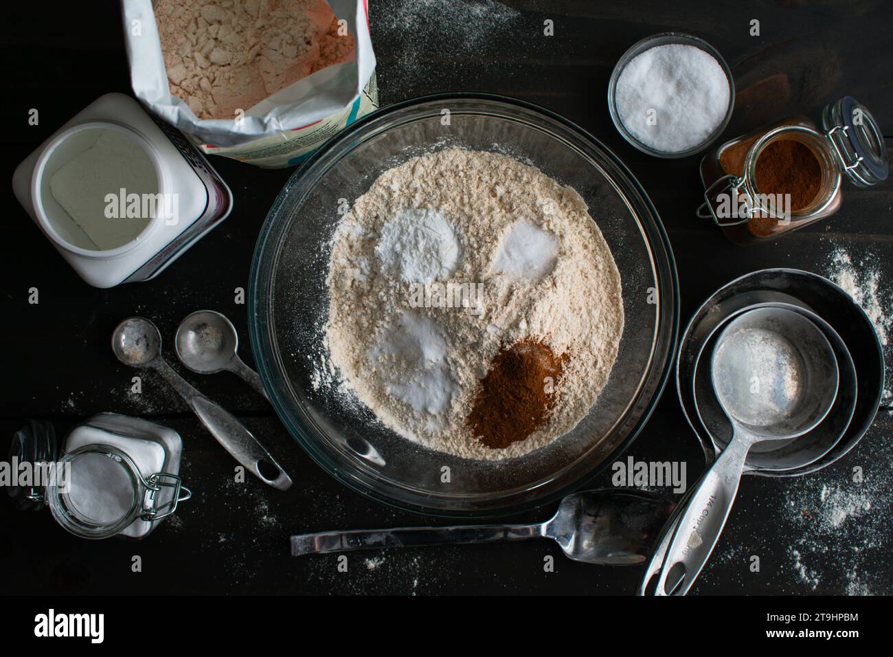 Mixing Dry Ingredients for Baked Apple Cider Donuts: Whole-wheat pastry flour in a glass mixing bowl surrounded by kitchen tools and ingredients Stock Photo