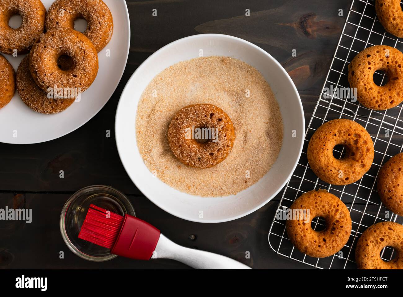 Dipping Baked Apple Cider Donuts in Cinnamon Sugar: Baked doughnut in a shallow bowl full of organic cane sugar and ground cinnamon Stock Photo