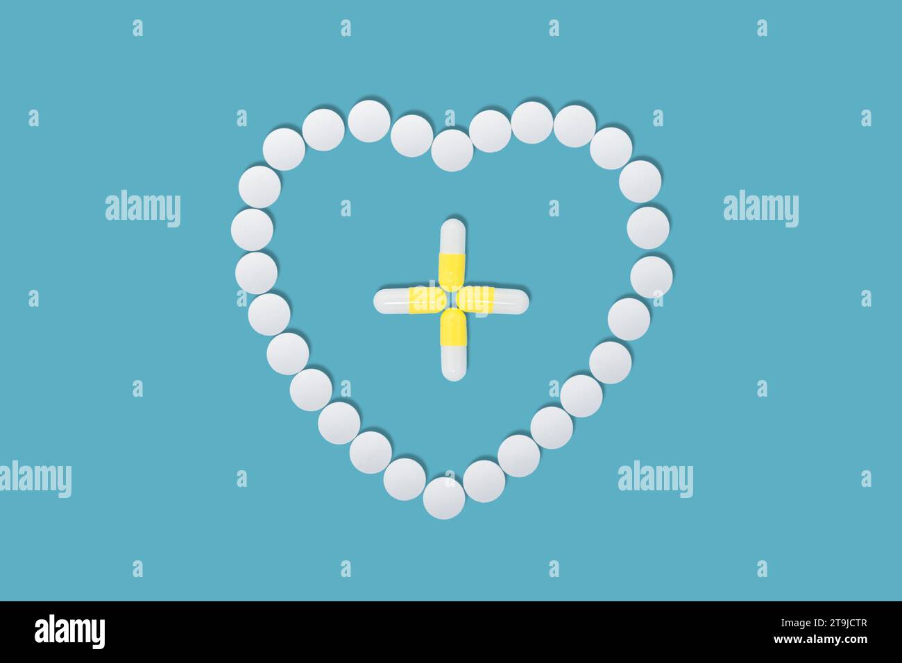 Scattered heart shaped pills abd yellow capsules in the form of a cross inside on soft light blue background, flat lay. Stock Photo