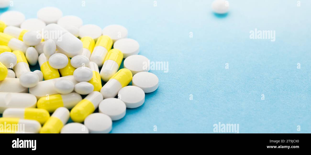 White and yellow pills and capsules were scattered on the table with copy space. Medical, pharmacy remedies background. Home medicine chest. Stock Photo