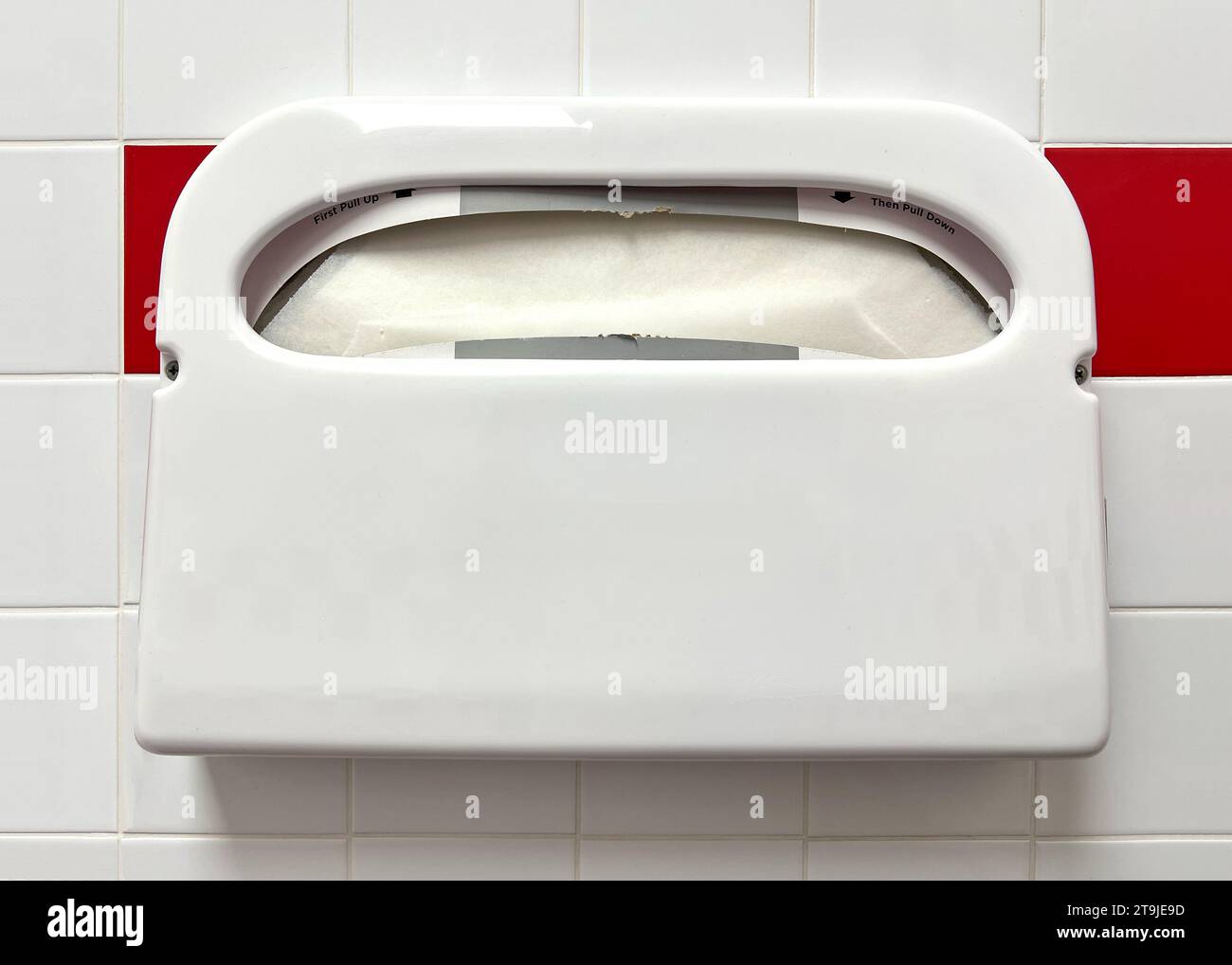 Paper toilet seat cover dispenser on red and white tile wall. Hygiene supplies for public