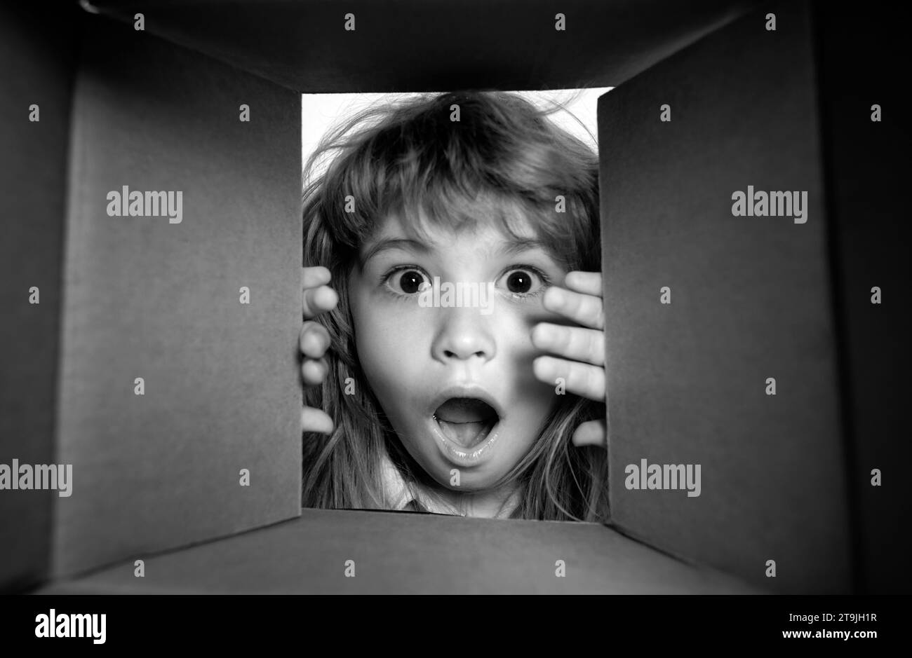 The surprised child unpacking, opening carton box and looking inside. The package, delivery, surprise, kids gift concept. Closeup kids face. Stock Photo