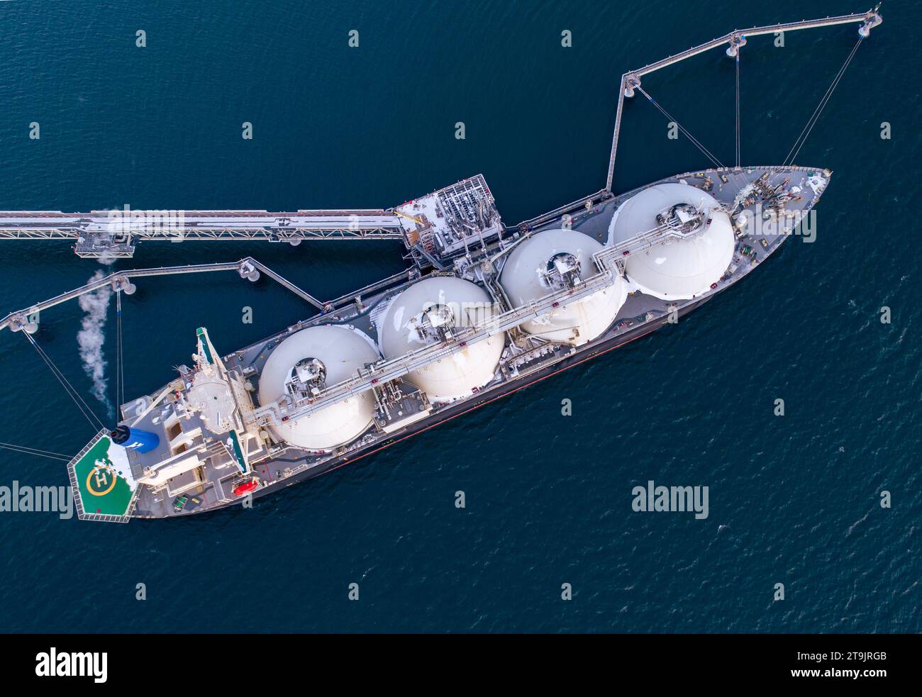Aerial of Liquified Natural Gas LNG carrier moored to a small gas terminal. Fuel crisis. Sanctions. Top down shot. Stock Photo