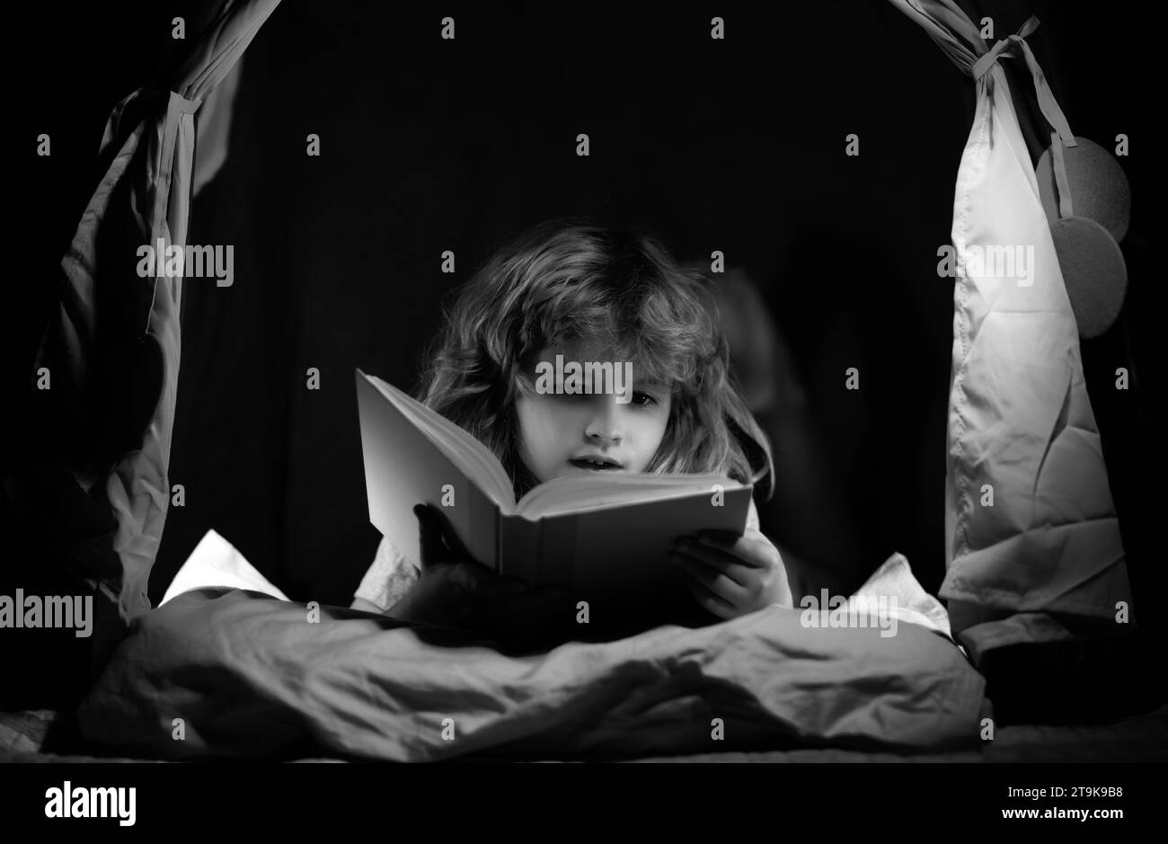 Kid boy in kids tent reading books. Kids face with night light. Concept