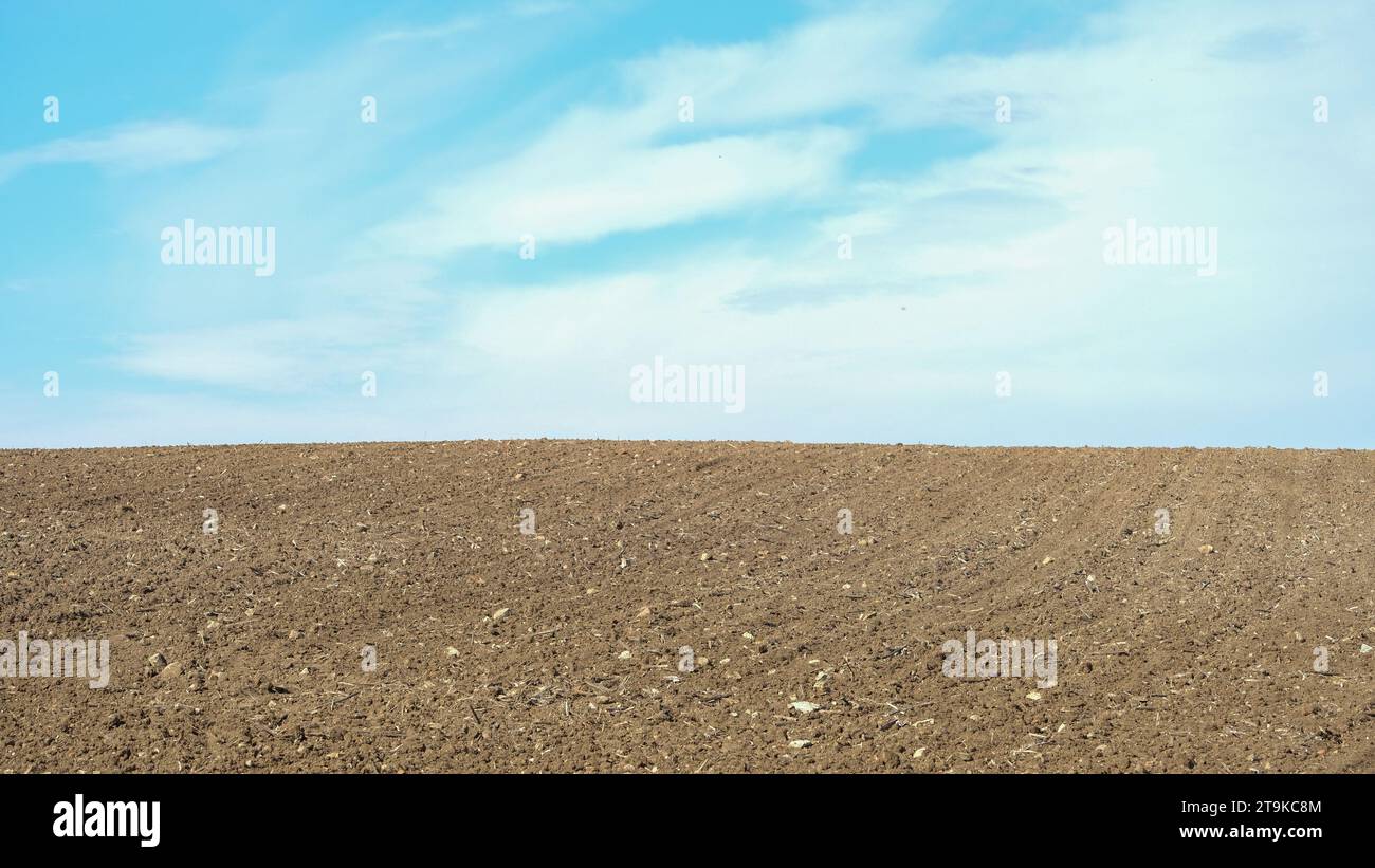 Ploughed farm field under a clear cloudy blue sky in an agricultural landscape. Open space area. Stock Photo