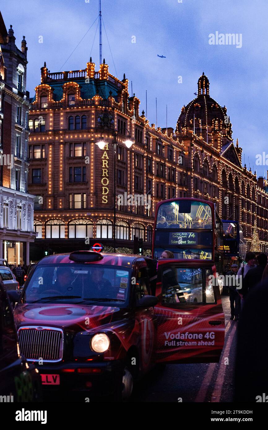Knightsbridge during an early winters evening with Harrods in the background and a open door red taxi Stock Photo