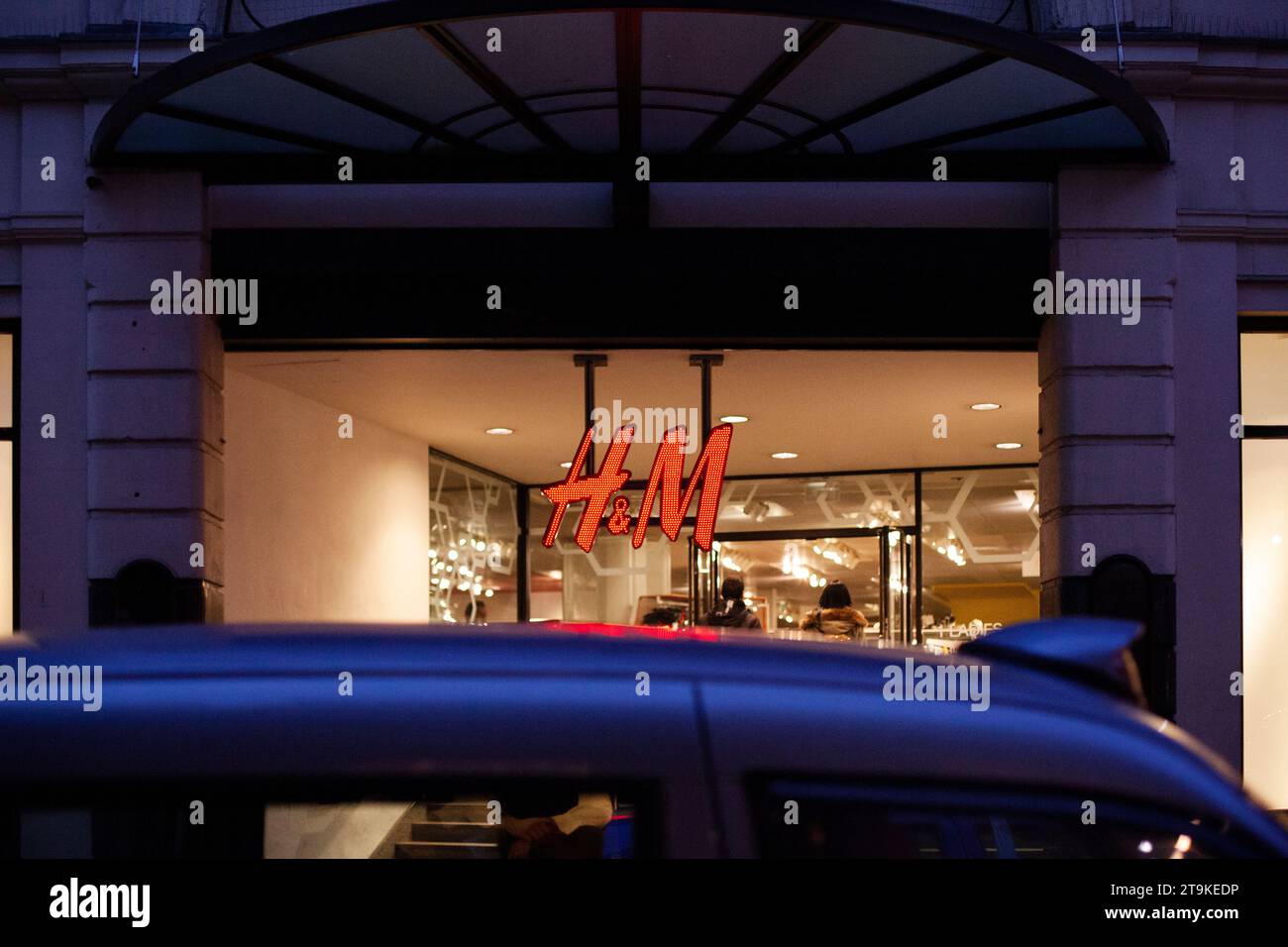 H&M Regent Street London shop front lit up at night frames by the top of a taxi driving past Stock Photo