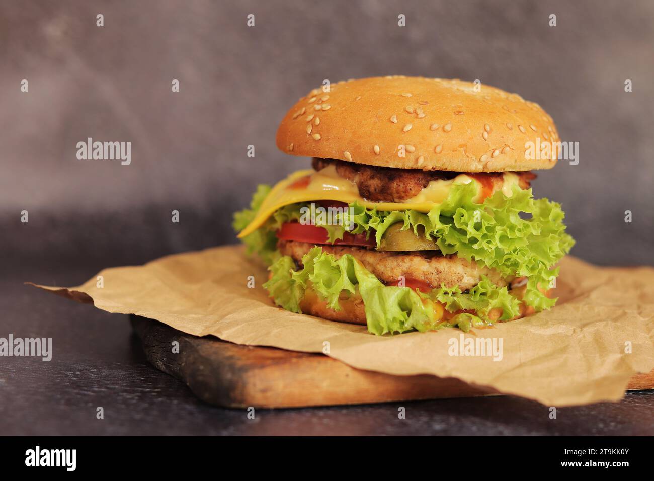 Double cheeseburger on a gray background. Juicy tasty burger on craft paper, side view. Fast food. Copy space Stock Photo