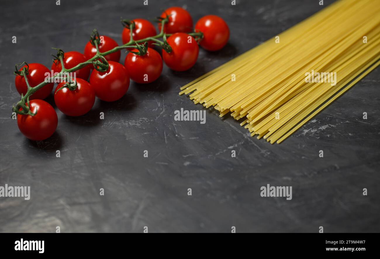 Cherry tomatoes branch and raw spaghetti - ingredients for making Italian pasta, on dark background, selective focus. Stock Photo