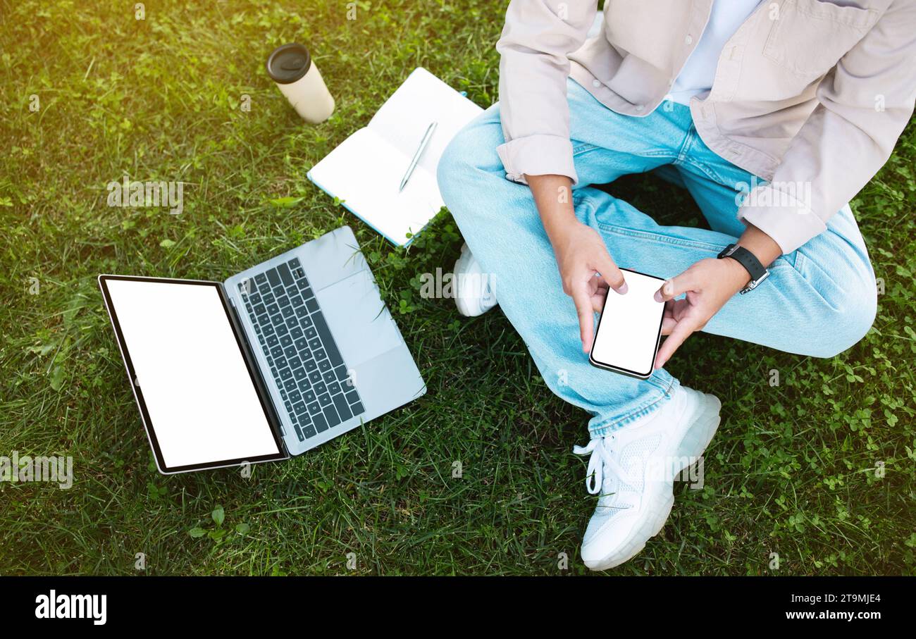 Asian man sitting on grass while using phone and laptop Stock Photo