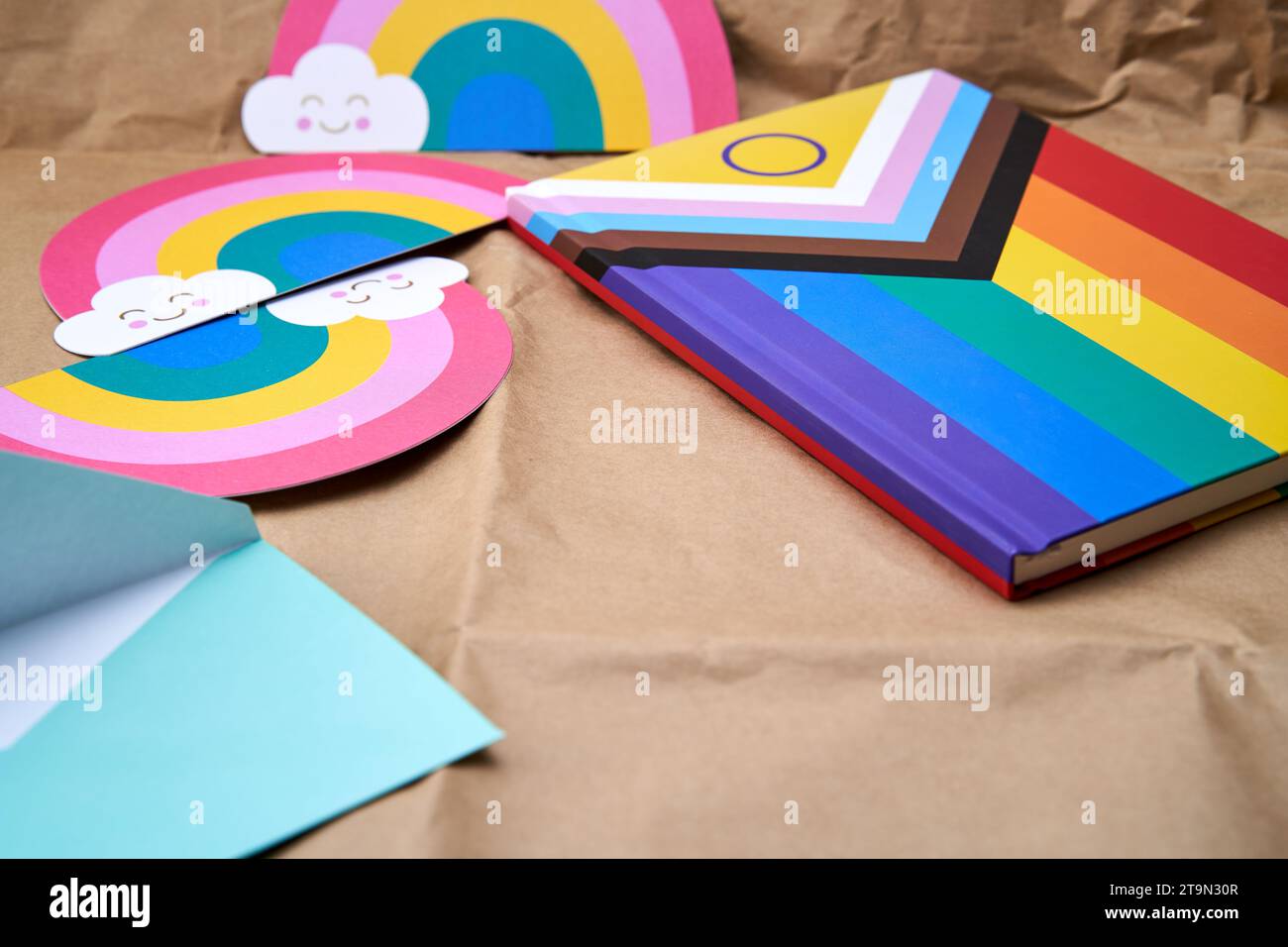 Close-up of a blue envelope on a cardboard surface and in the background a notebook with the lgbtiq+ flag and several rainbows. Stock Photo