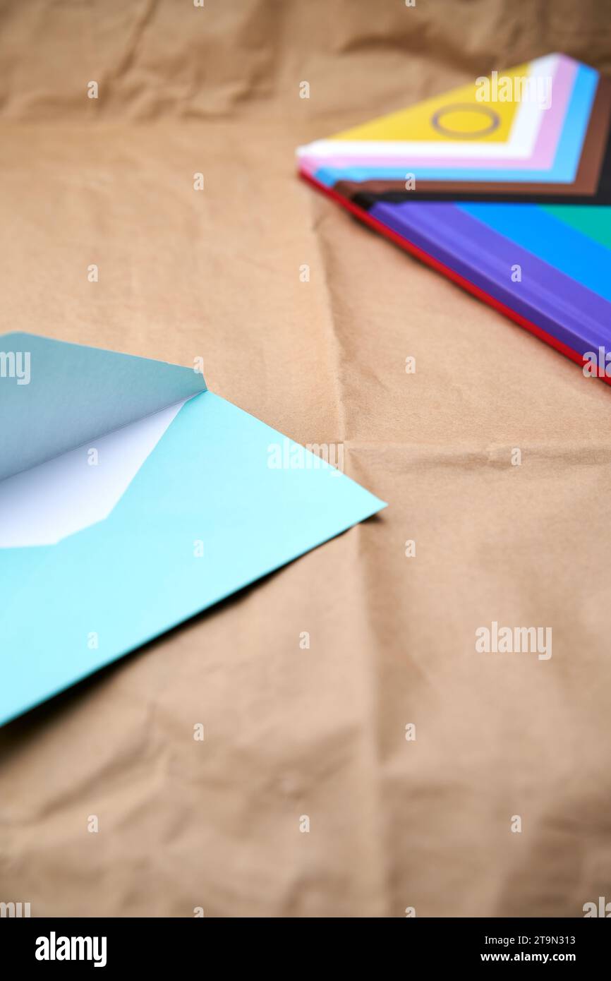 Close-up of a blue envelope on a cardboard surface and in the background out of focus a notebook with the lgbtiq+ flag. Stock Photo