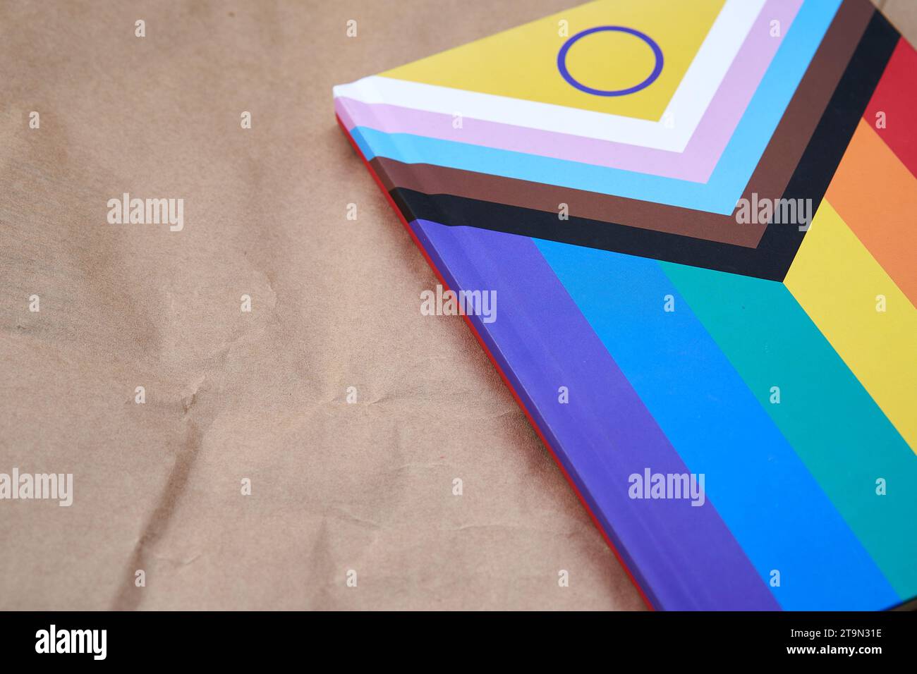 Notebook with the lgbtiq+ flag on a cardboard texture background. Stock Photo