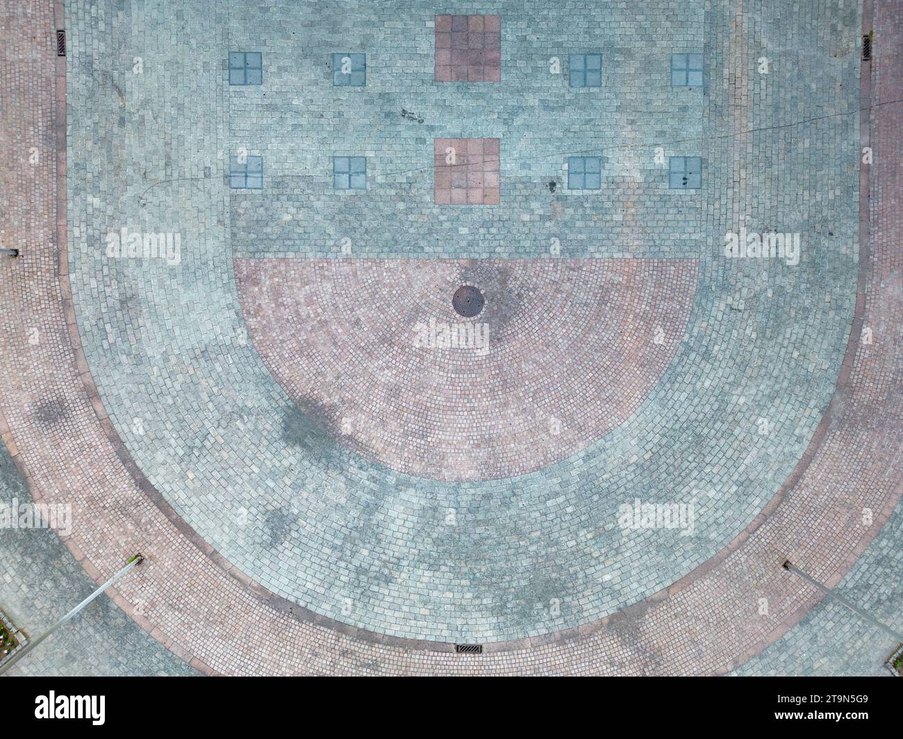 This image provides an aerial perspective of a sports court, seemingly worn by time and use. The faded markings and weathered surface speak to the many games and events that have taken place here. At the center, the basketball hoop casts a solitary shadow, standing as a silent witness to the court's history. The surrounding area appears to be in a state of disrepair or construction, adding a layer of intrigue to the urban scene. Urban Canvas: Aerial View of a Sports Court. High quality photo Stock Photo