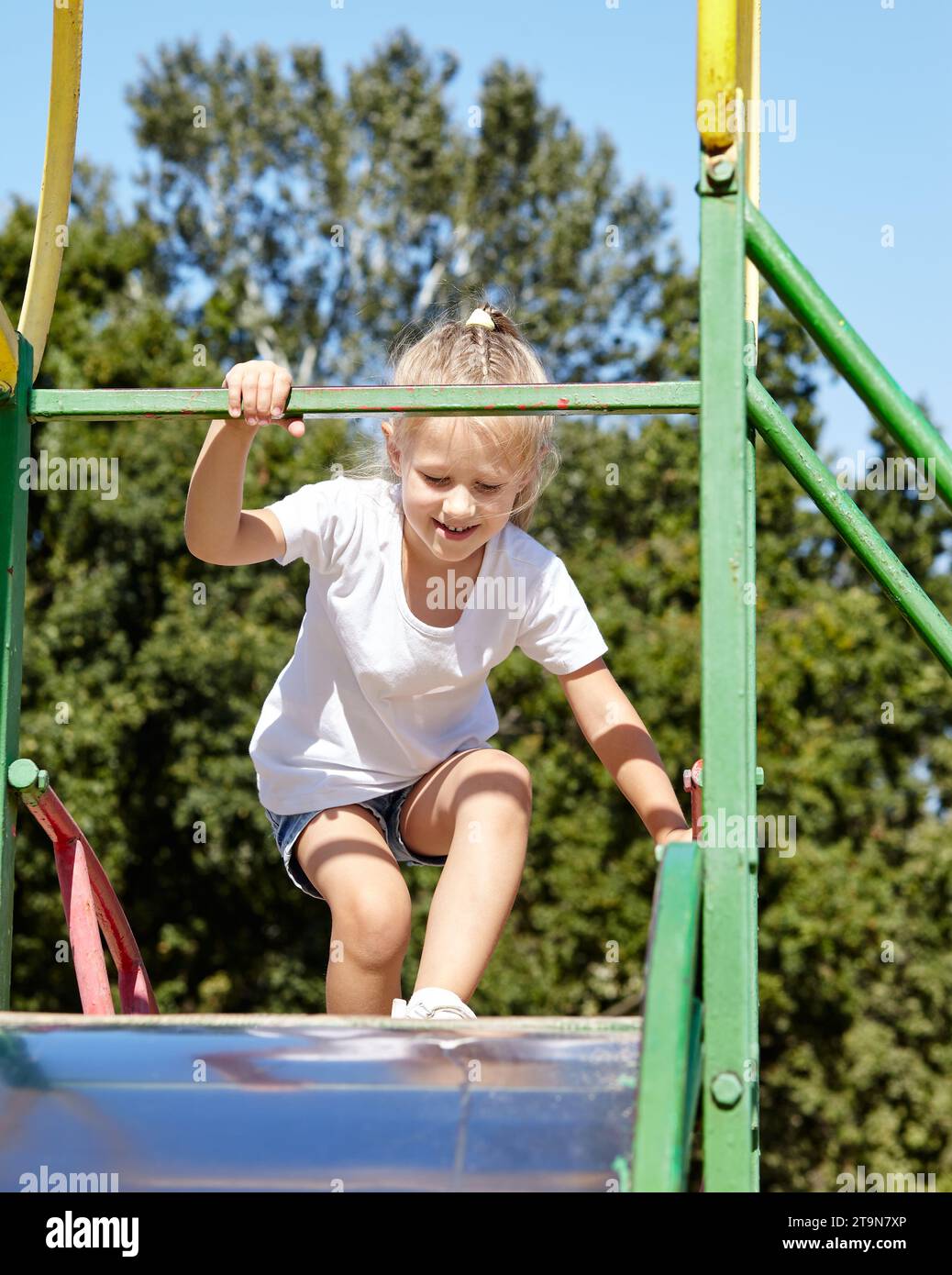 Little girl playing on a slide in a playground in the summer city park ...