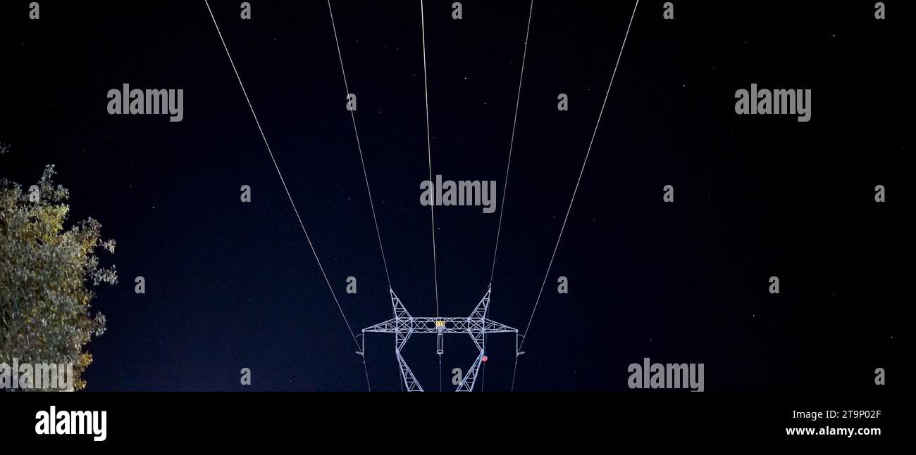 nighttime image of part of a pole and high-voltage cables against a