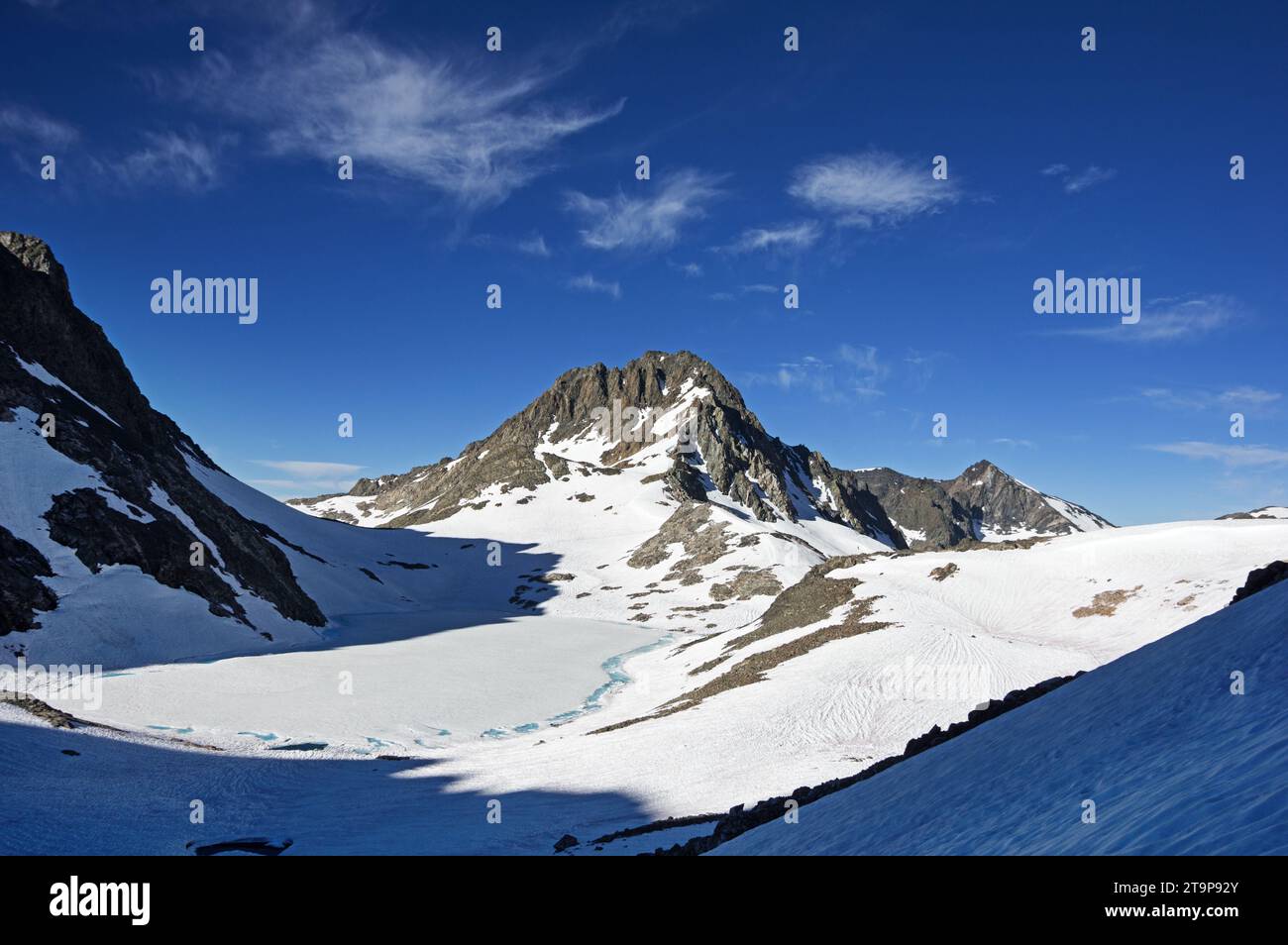 Charybdis Mountain rises above a mostly frozen Lake 11828 in the Ionian Basin of Kings Canyon National Park in July of a high snow year Stock Photo