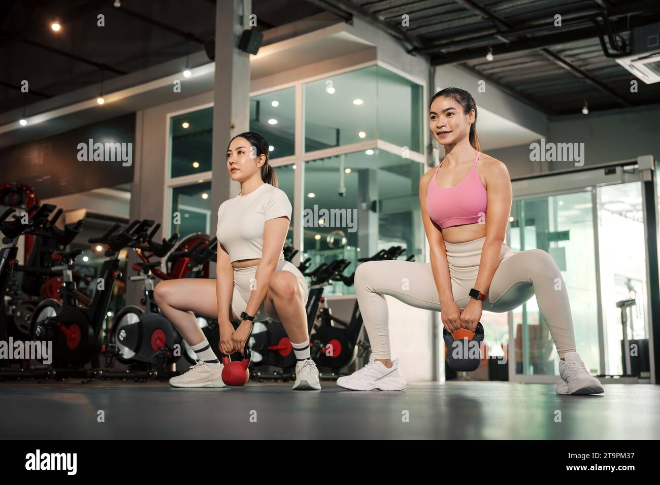 Two Young Asian woman exercise workout at gym fitness training sport with kettlebell weight lifting. Stock Photo