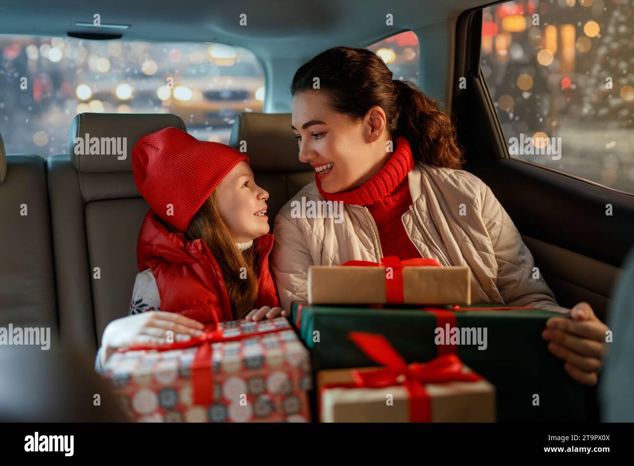 Woman and her child  holding presents and delivering them on car to home. Holidays concept. Time of Christmas Eve. Stock Photo