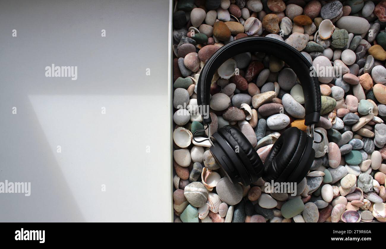 Concept Photo Of Flat Box Filled With Pebbles And Black Headphones On It On A White Surface Stock Photo