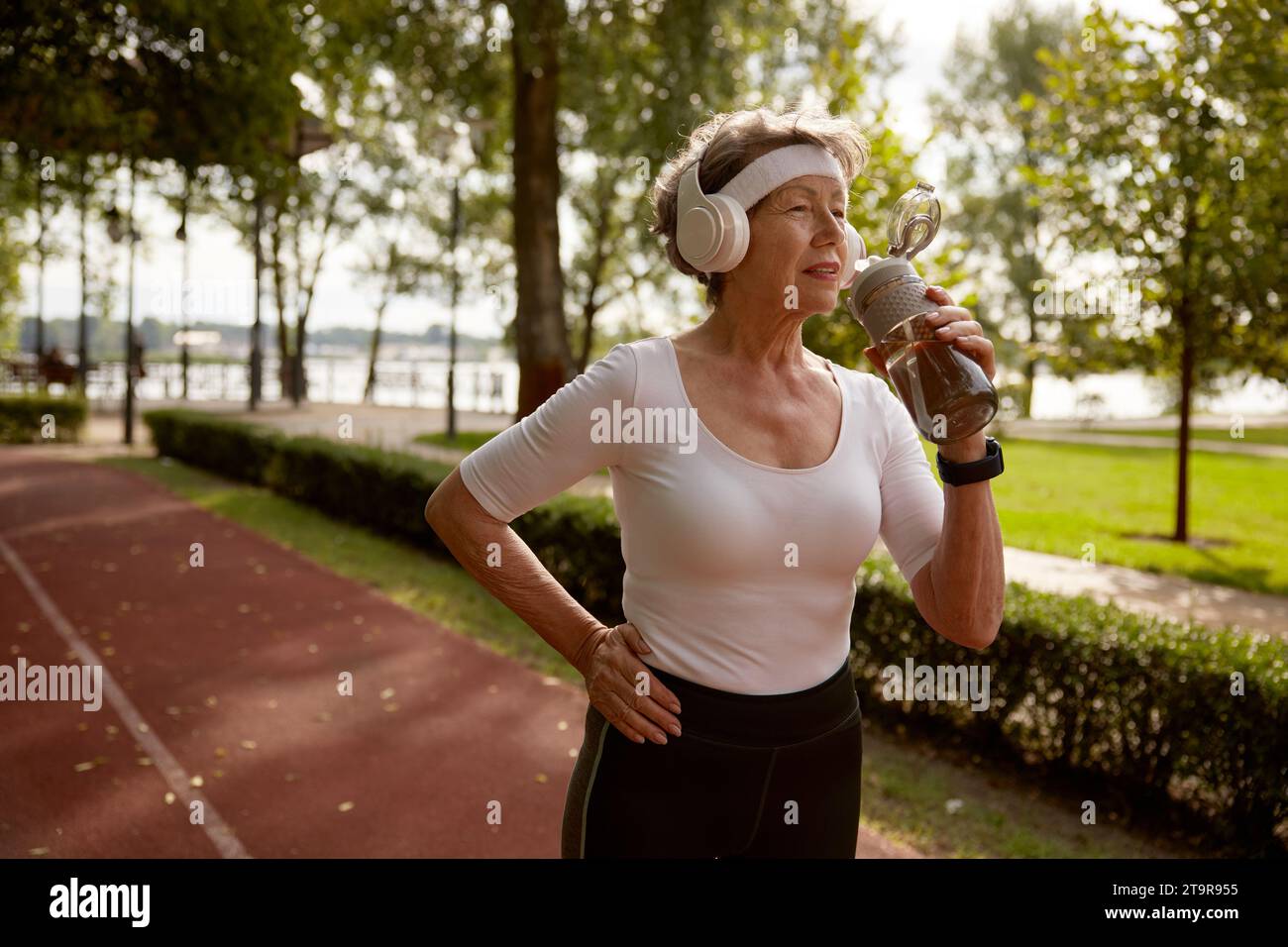 Elderly woman drinking water taking short break during running exercise Stock Photo